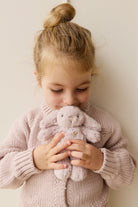 Girl holding a plush rabbit, wearing a pink knitted cardigan.