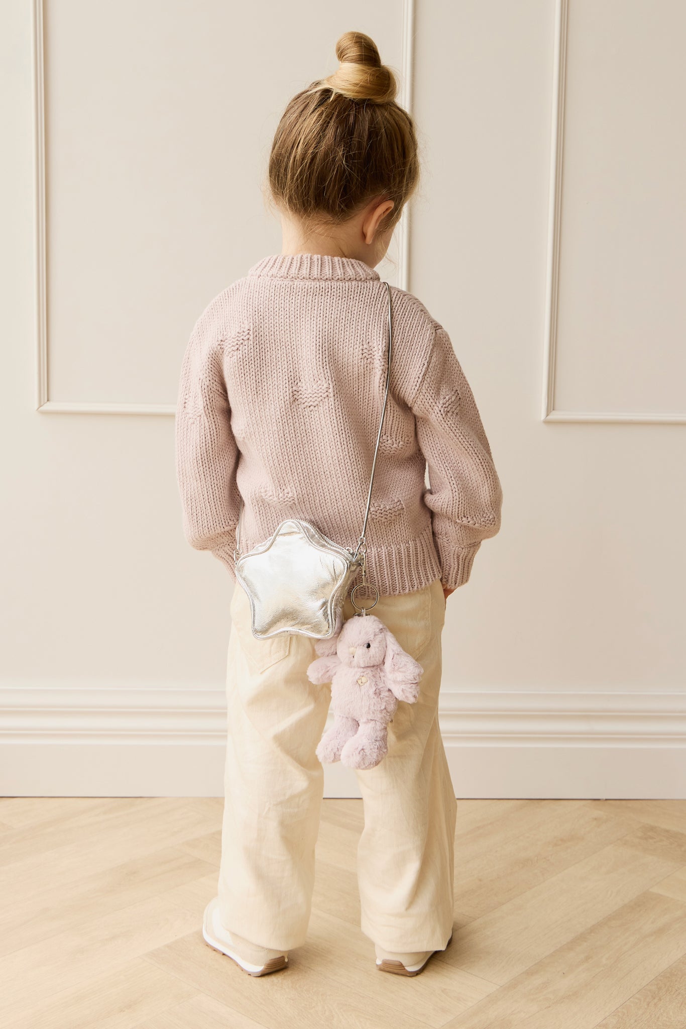 Back view of girl in pink sweater and tan pants, wearing a star purse with a bunny charm.