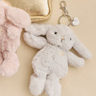Close-up of a pink and gray plush bunny keychain next to a small gold purse on a beige surface.