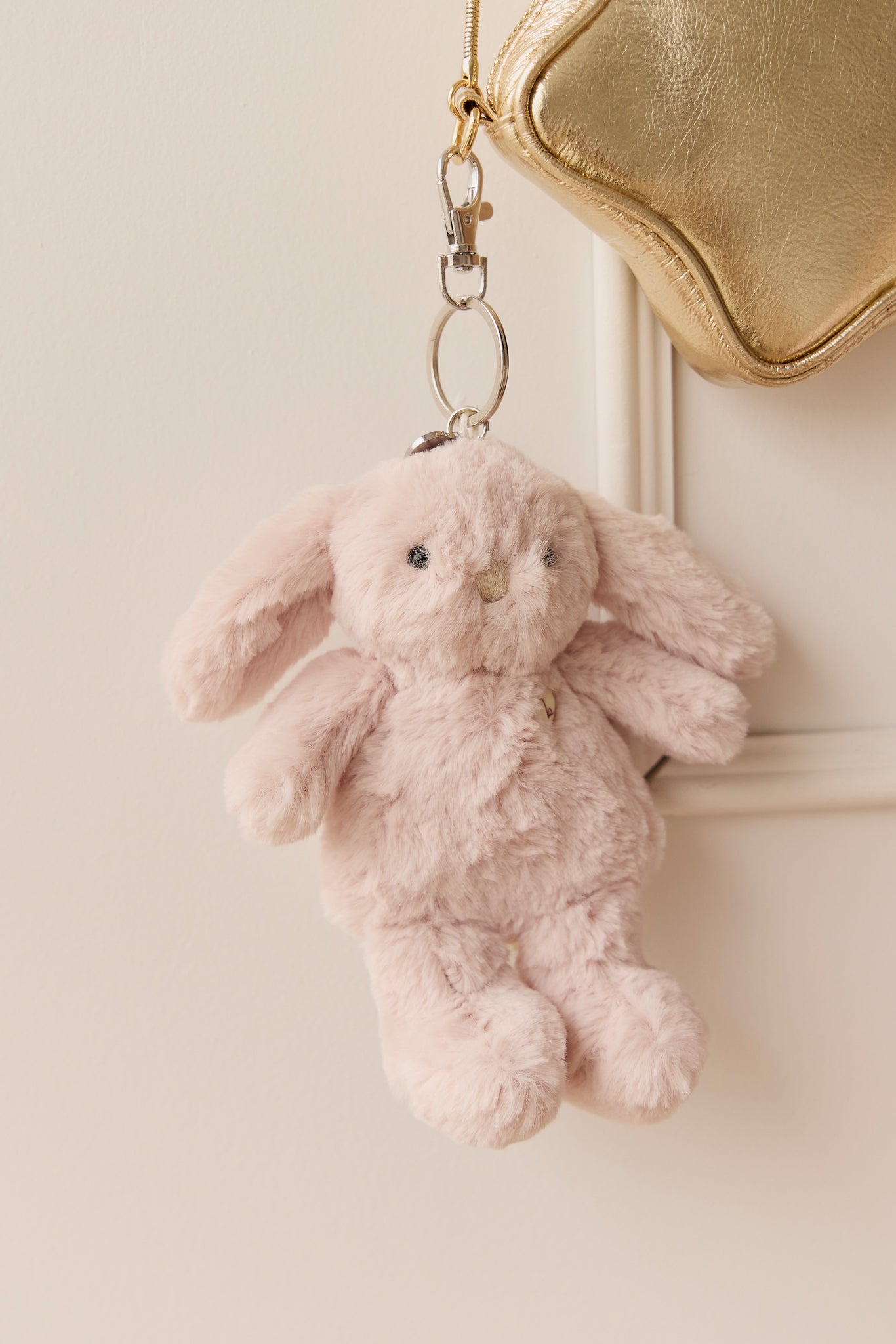Pink plush bunny keychain hanging from a gold bag.