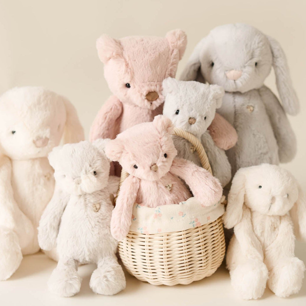 Collection of soft toys including teddy bears and bunnies in a wicker basket on a light background
