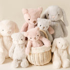 Soft pink and white plush bear and bunny toys by Snuggle Bunnies, arranged in a wicker basket with floral lining, lifestyle shot