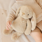 Child holding a plush bunny toy with a soft beige background