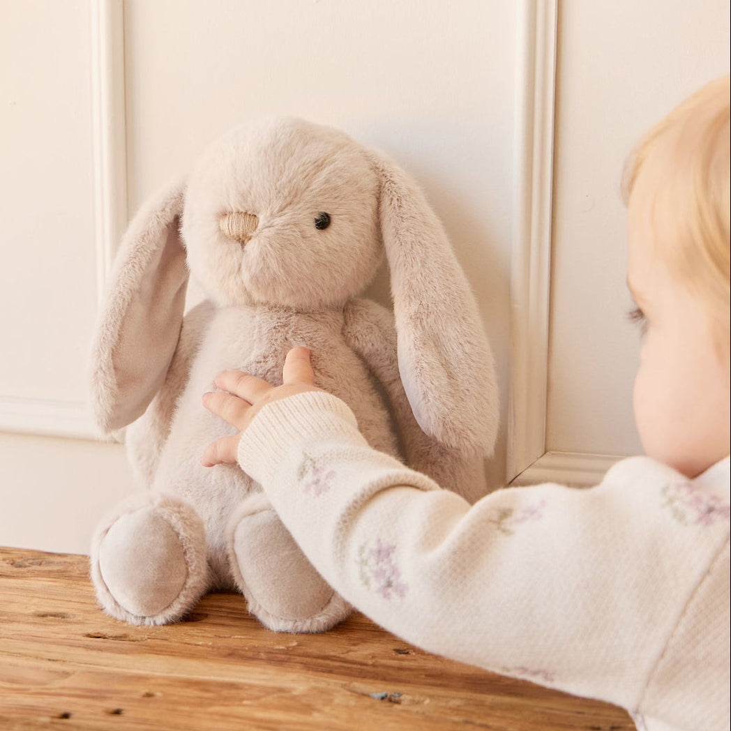 Stuffed bunny on wooden bench with child's hand reaching.