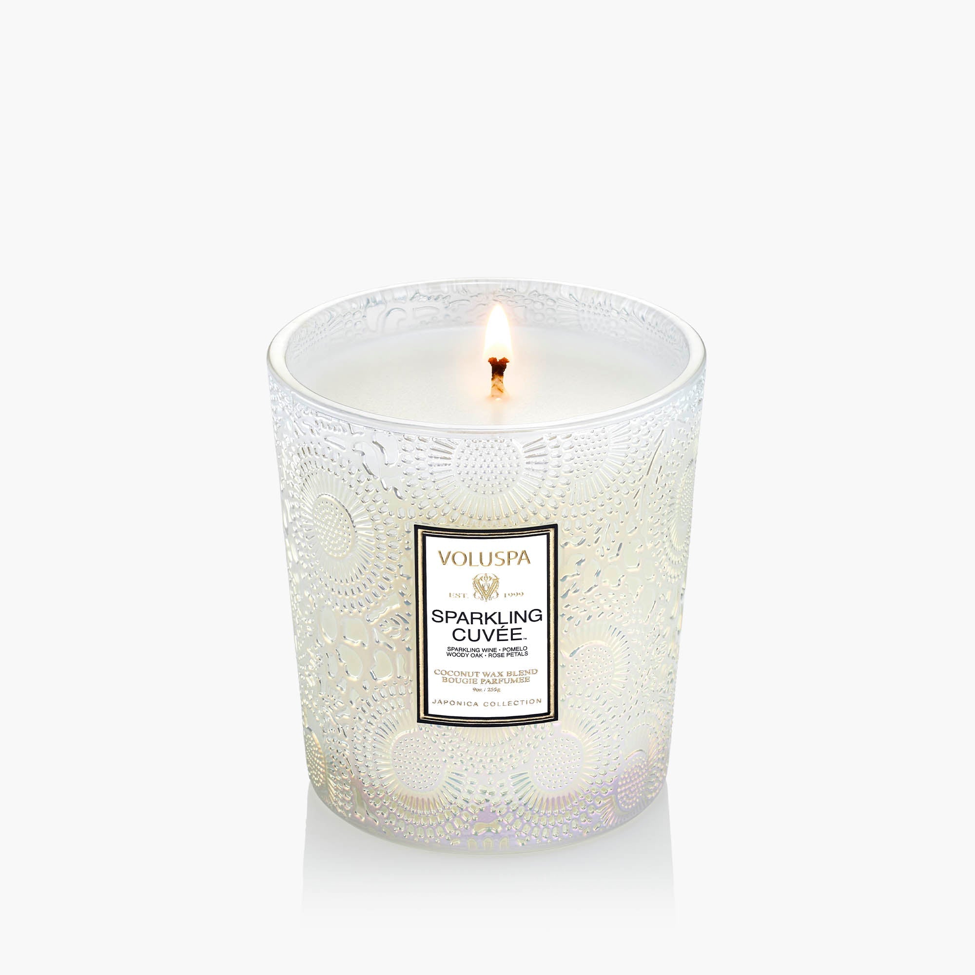 Lit candle in a decorative glass container with 'Voluspa' branding on a white background