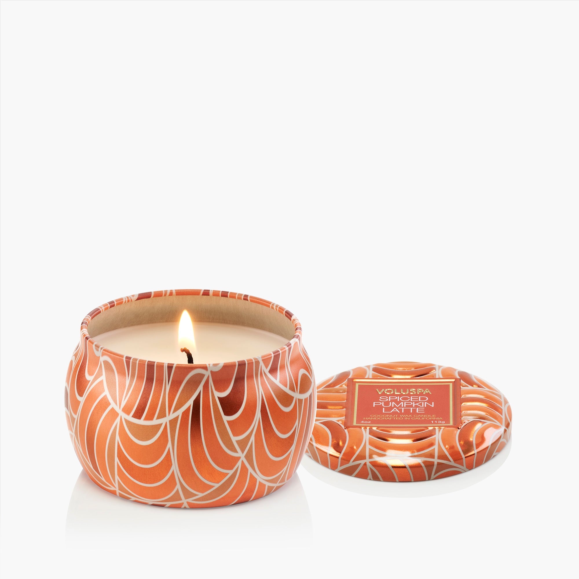 Candle in an orange and white patterned container with a lit flame on a white background