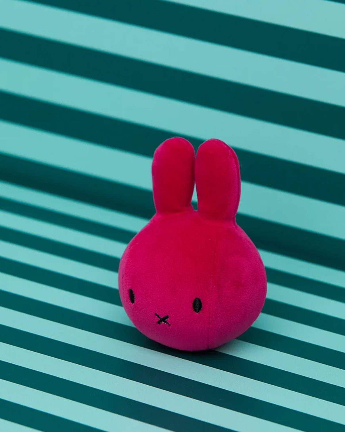 Pink plush toy with bunny ears on a striped green and blue background