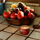 Fruit bowl with tomatoes and a lit candle on a tiled surface