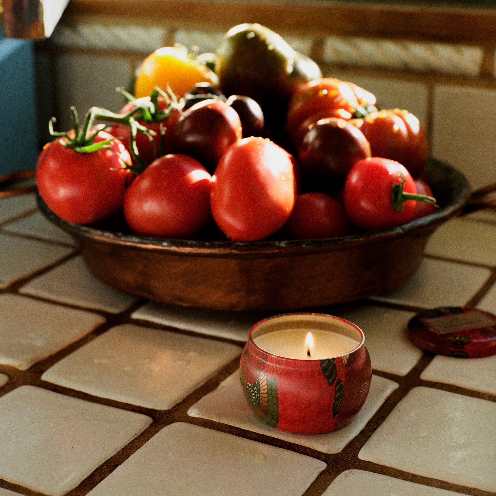Fruit bowl with tomatoes and a lit candle on a tiled surface