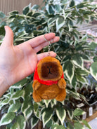 Hand holding a brown plush keychain with a red scarf.
