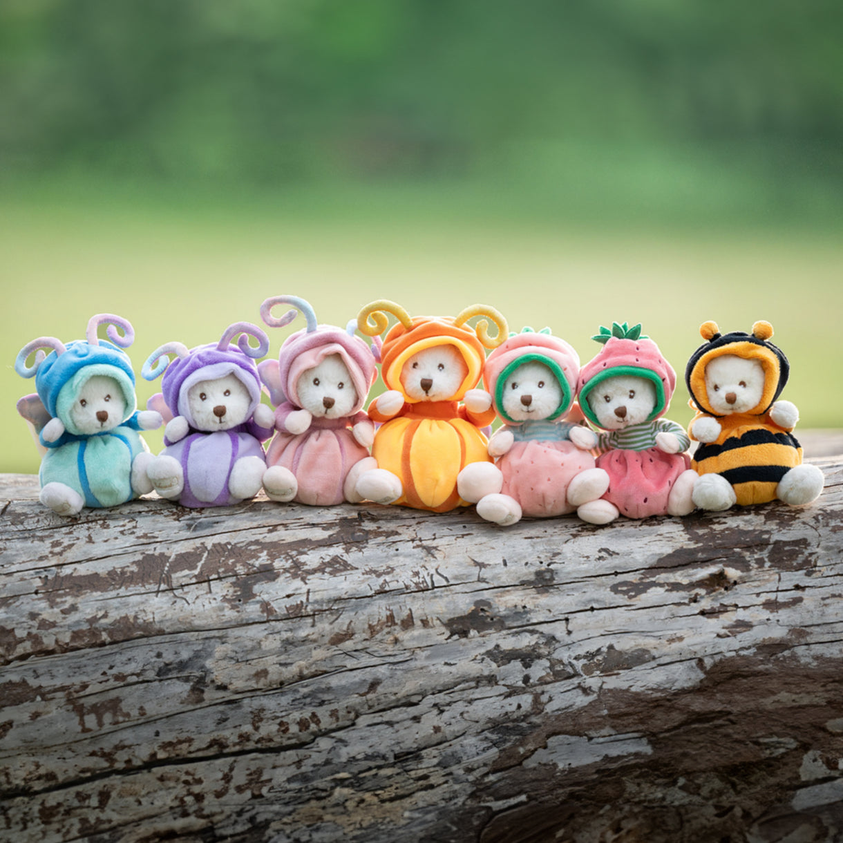 Colorful teddy bear toys in various costumes on a wooden log with a green blurred background