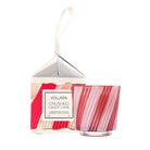 Voluspa Crushed Candy Cane hand-blown glass candle in a pink striped glass jar, shown next to its white and red patterned packaging box with a hanging loop on a white background.