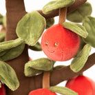 Plush toy apple with a face on a branch with green leaves
