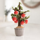 Plush toy tree with red apples in a pot on a blurred background