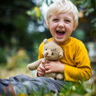 Child in a yellow shirt holding a teddy bear outdoors