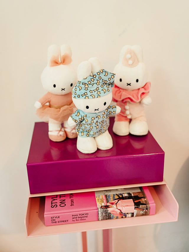 Three cartoon-style rabbit figurines on a pink shelf with books underneath.