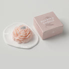 Peonie candle by Jellycup, sitting on a white ceramic dish next to its pink packaging box.