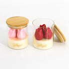 Two clear glass jars with bamboo lids on a white background, filled with cream-colored wax and decorated with pink and red tulip-shaped ornaments. One jar is closed, and the other is open with its lid leaning against it.
