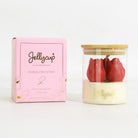 A Jellycup soy wax candle in a clear glass jar with a bamboo lid, shown next to its pink floral collection box. The candle features two red tulip-shaped wax flowers set in a creamy off-white wax base with gold foil branding.