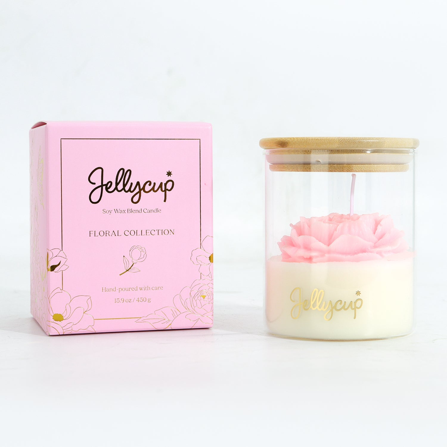 A pink and cream soy wax candle in a clear glass jar with a bamboo lid, shown next to its pink floral collection packaging box by Jellycup.
