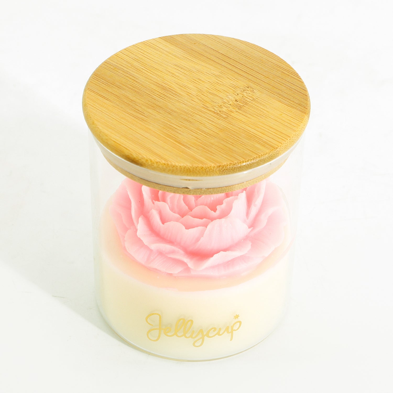 A clear glass jar candle with a light bamboo lid, containing a white wax base and a pink rose-shaped gel insert. The brand name 'Jellycup' is printed in gold on the front of the jar.