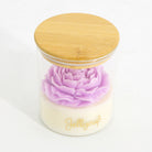 A clear glass jar candle with a light wood lid, featuring a layered design with a pale cream base and a prominent light purple flower on top. The brand name 'Jellycup' is printed in gold script on the front of the jar.