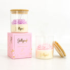 A Jellycup jar candle shown with its pink floral gift box and bamboo lid on a clean white background. One candle is closed in its glass jar with a bamboo lid and purple wax flower, resting on the pink box.