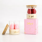 Two Jollycup scented candles in clear glass jars with bamboo lids, displayed alongside their pink branded box on a white background. One candle features pink tulip-shaped wax pieces, and the other features red tulip-shaped wax pieces.