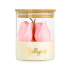 A clear glass jar candle with a bamboo lid, featuring two pink tulip-shaped wax flowers on a cream-colored wax base with gold 'Jellycup' branding.