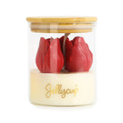 A Jellycup jar candle with a clear glass body, a light wood lid, and a cream-colored wax base featuring two red tulip-shaped wax flowers and gold script branding.