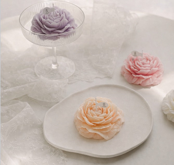 Floral-shaped candle by Jellycup with a decorative paper flag, sitting on a plate near lace fabric.