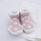 Pair of pink baby shoe-socks with white flowers on white fabric.