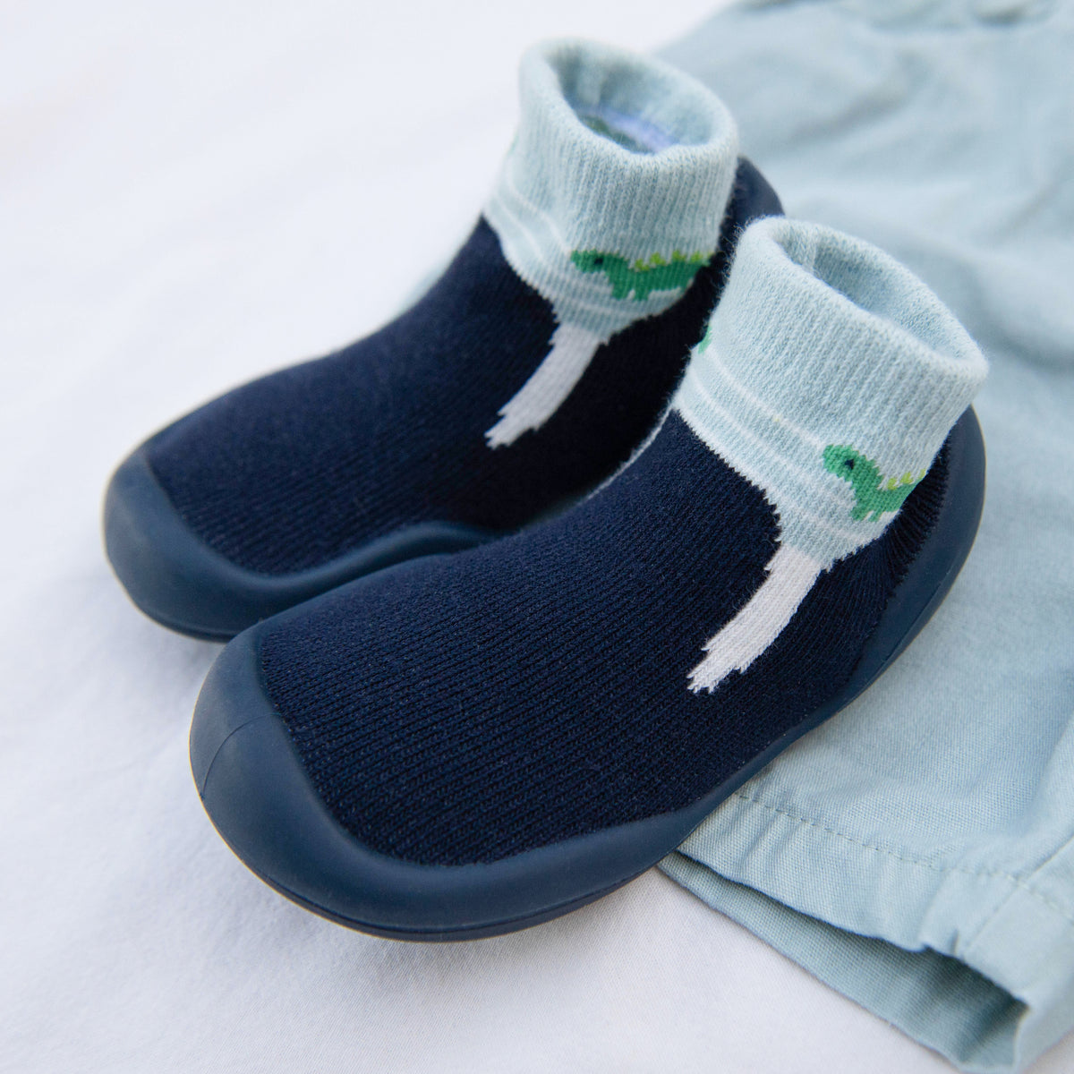 Pair of blue baby slipper socks on a white surface with a blue shirt next to them.