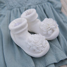 White baby shoes with fabric flowers on a light blue fabric background.