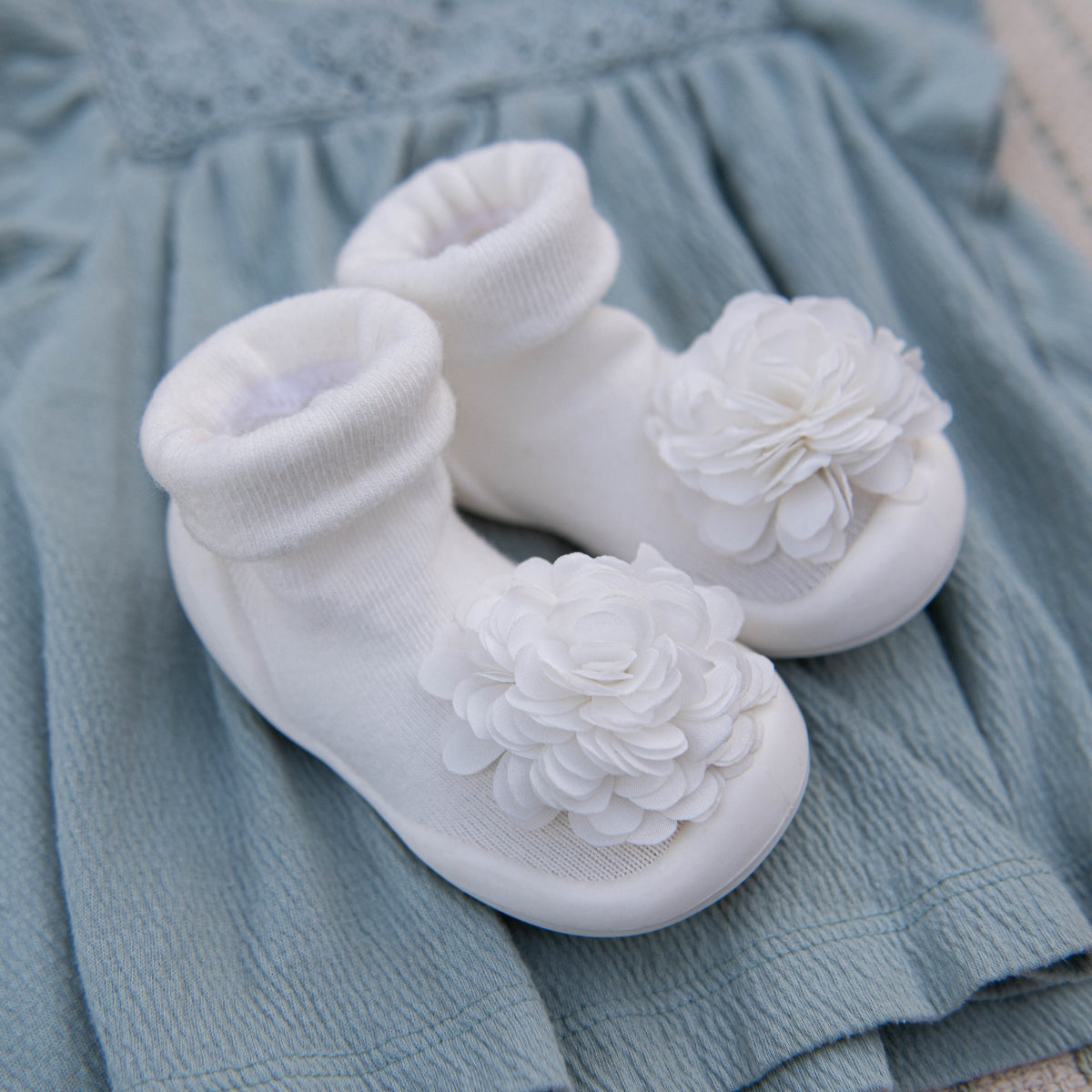 White baby shoes with fabric flowers on a light blue fabric background.