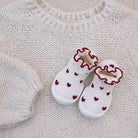 White baby shoes with red heart patterns on a beige knitted surface