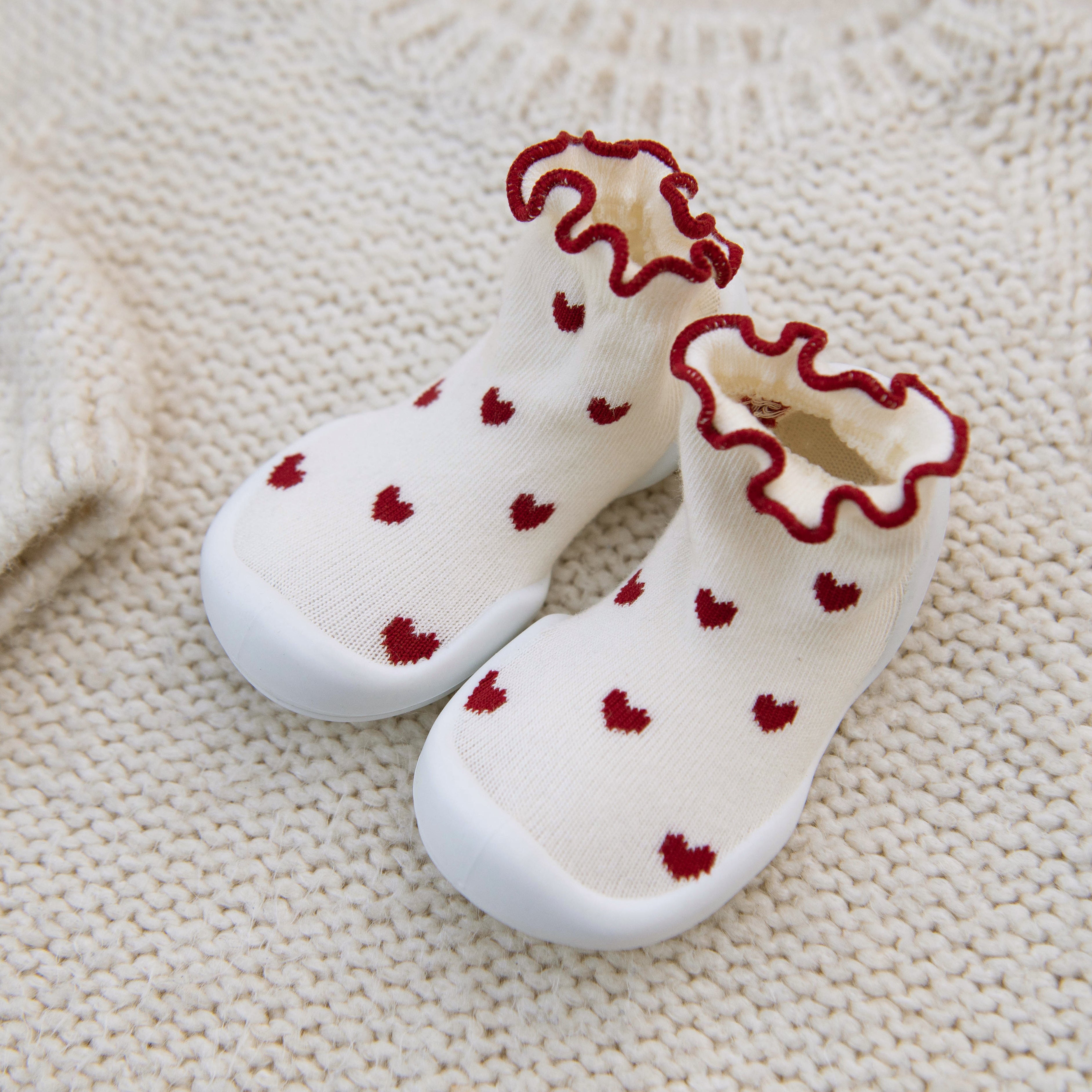 White socks with red hearts and ruffled edges on a textured beige surface