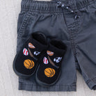 Black slippers with sports-themed designs on a gray fabric surface