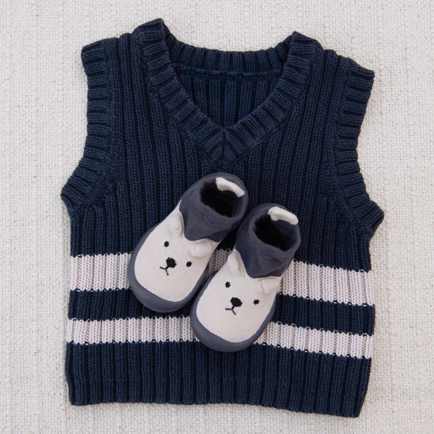 Navy and white striped sweater vest with cartoon shoes on a textured surface