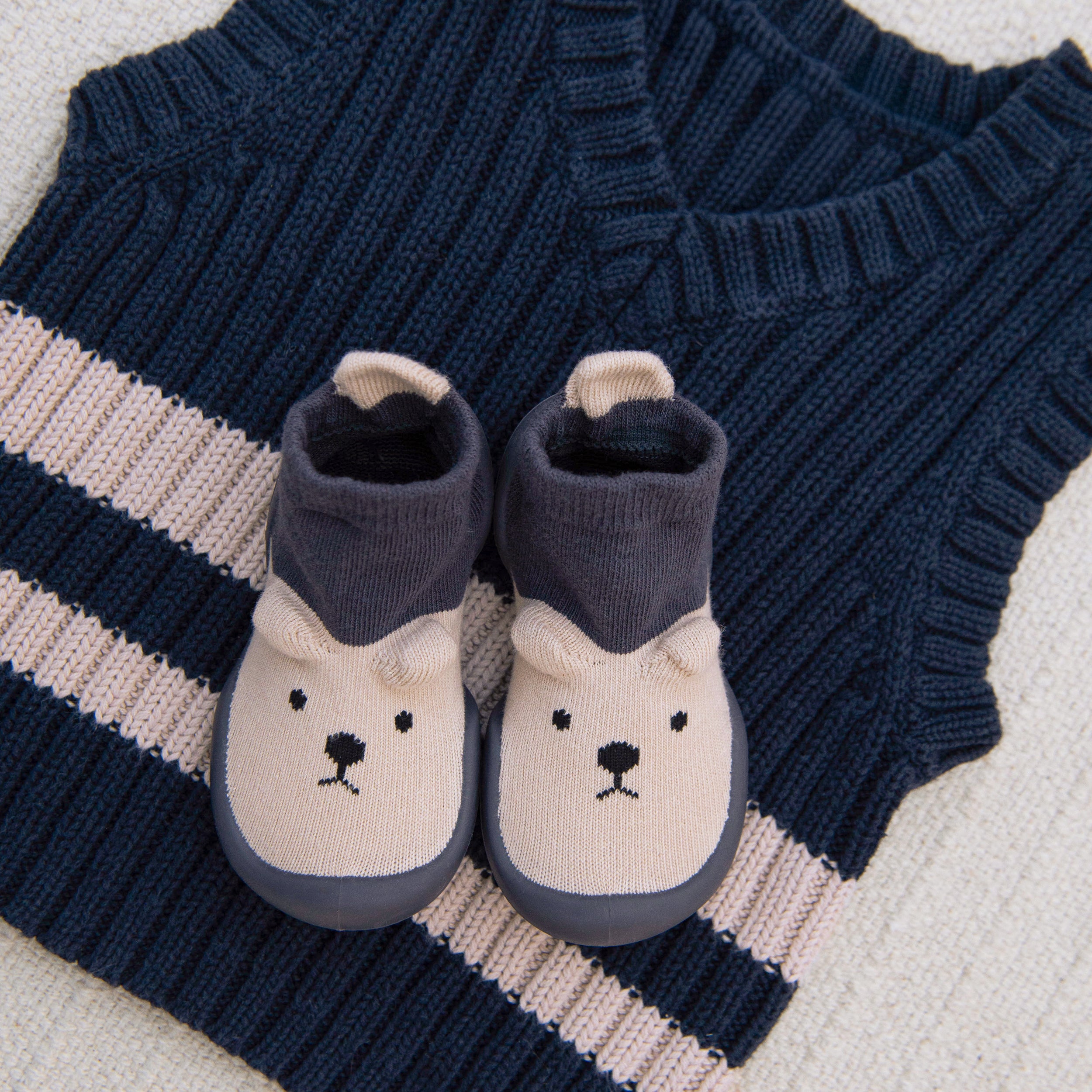 Pair of baby booties with bear design on a knitted navy and white fabric background