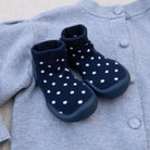Navy blue baby boots with white polka dots on a light gray sweater.