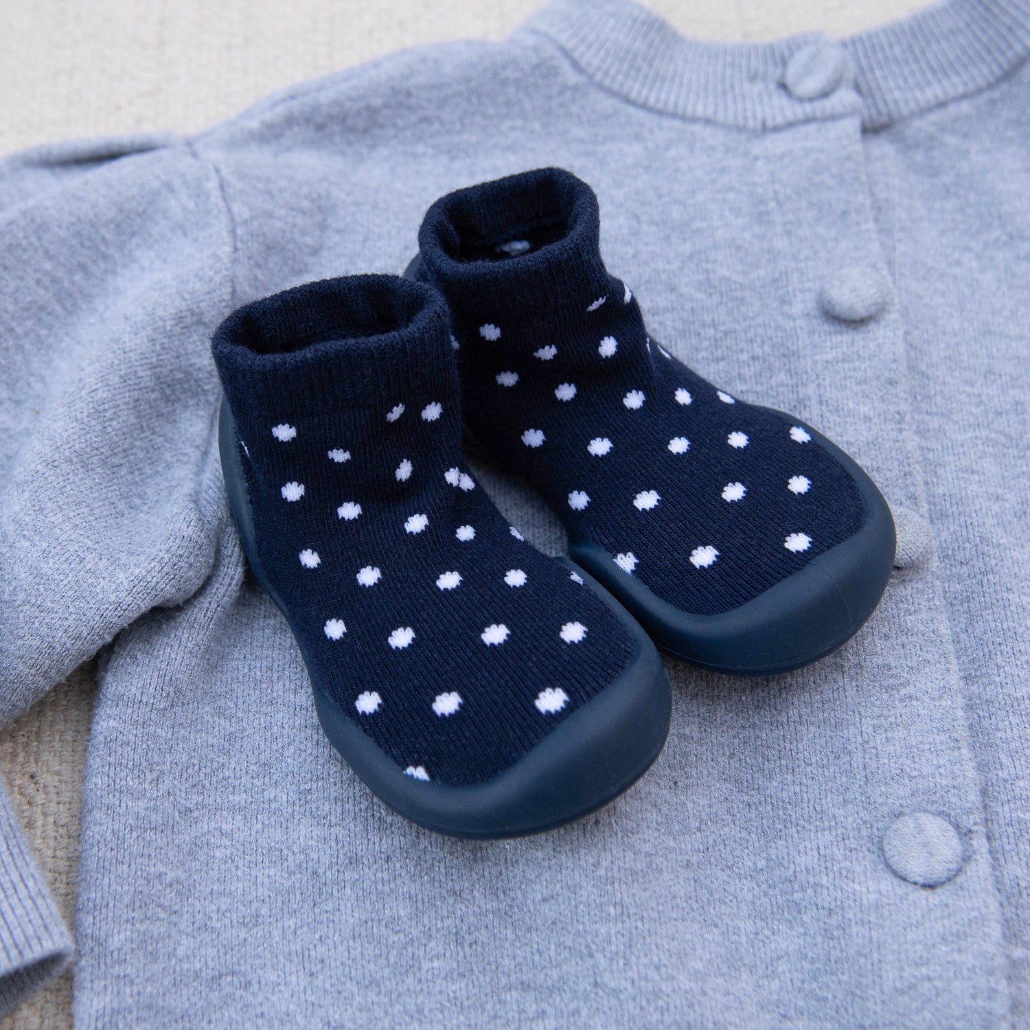 Navy blue baby boots with white polka dots on a light gray sweater.