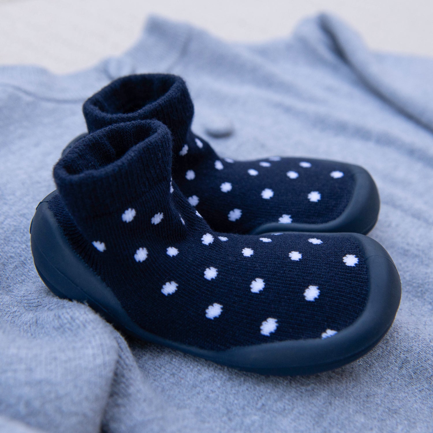 Pair of navy blue socks with white polka dots on a light gray fabric background