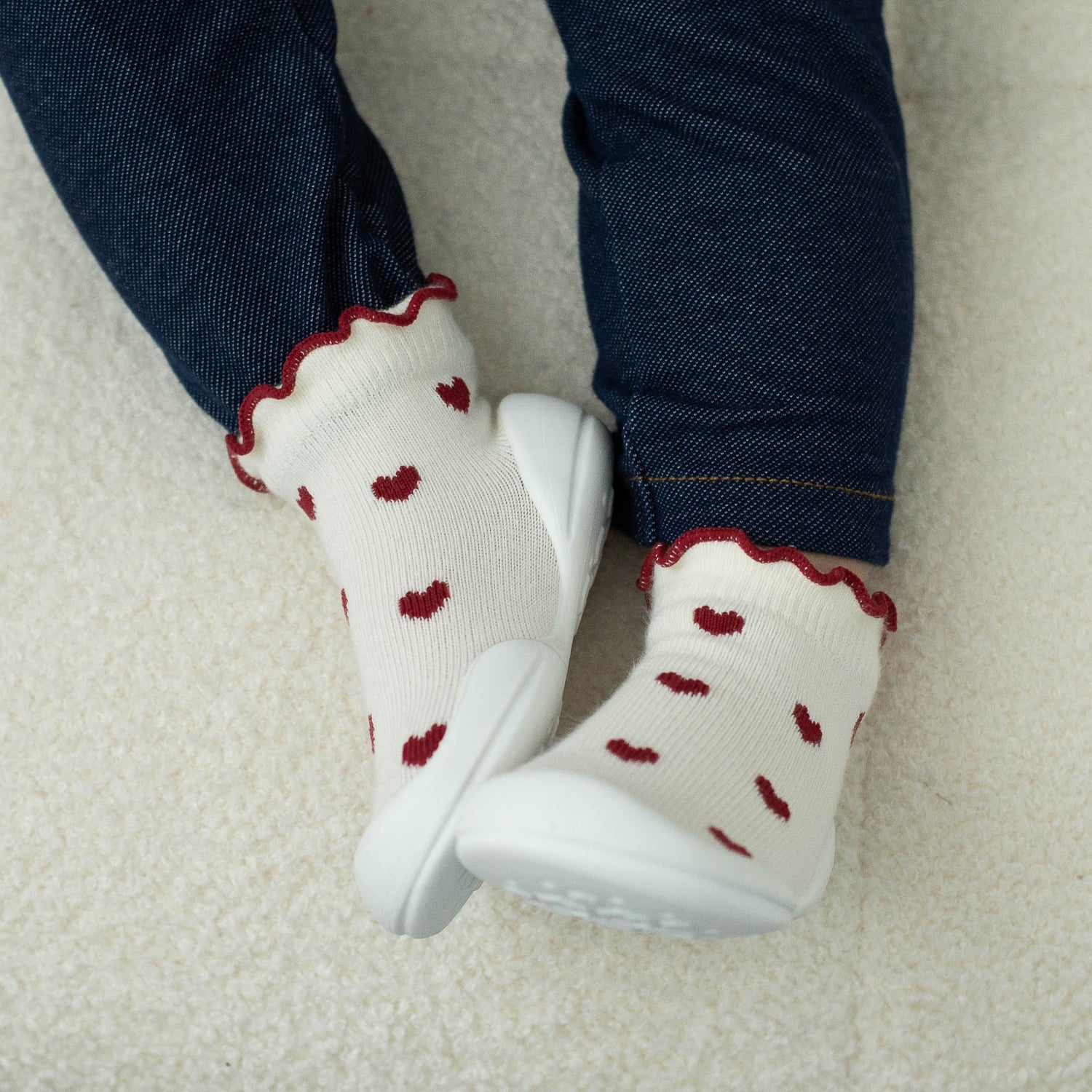 White socks with red heart patterns worn by a child, standing on a light-colored carpet.