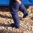 Child's legs in blue pants and shoes on a playground surface with wood chips.