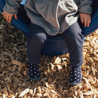 Child sitting on a blue slide with feet in polka dot socks on wood chips