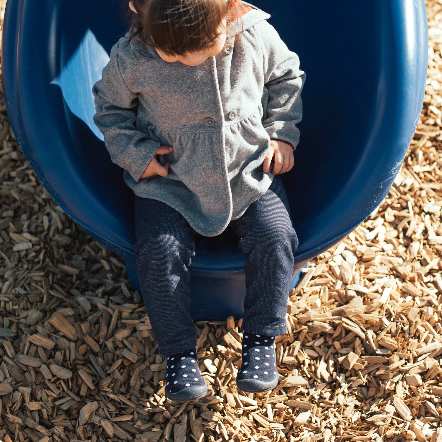 Child sitting on a blue playground tube slide with wood chips below