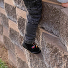 Person wearing black shoes with colorful designs on a stone wall