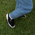 Person wearing black and white sneakers with blue pants on grass