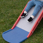 Child sliding down a blue and red slide on grass